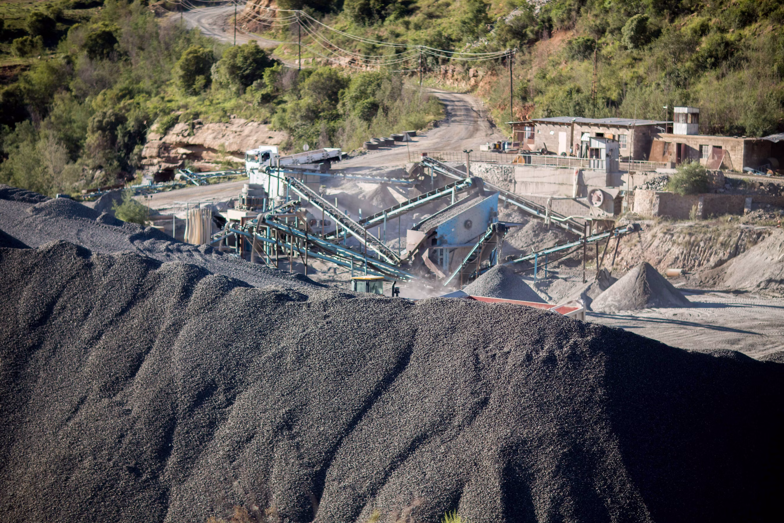 Industrial mineral crushing and screening facility with conveyor transfer chutes and large graded stockpile