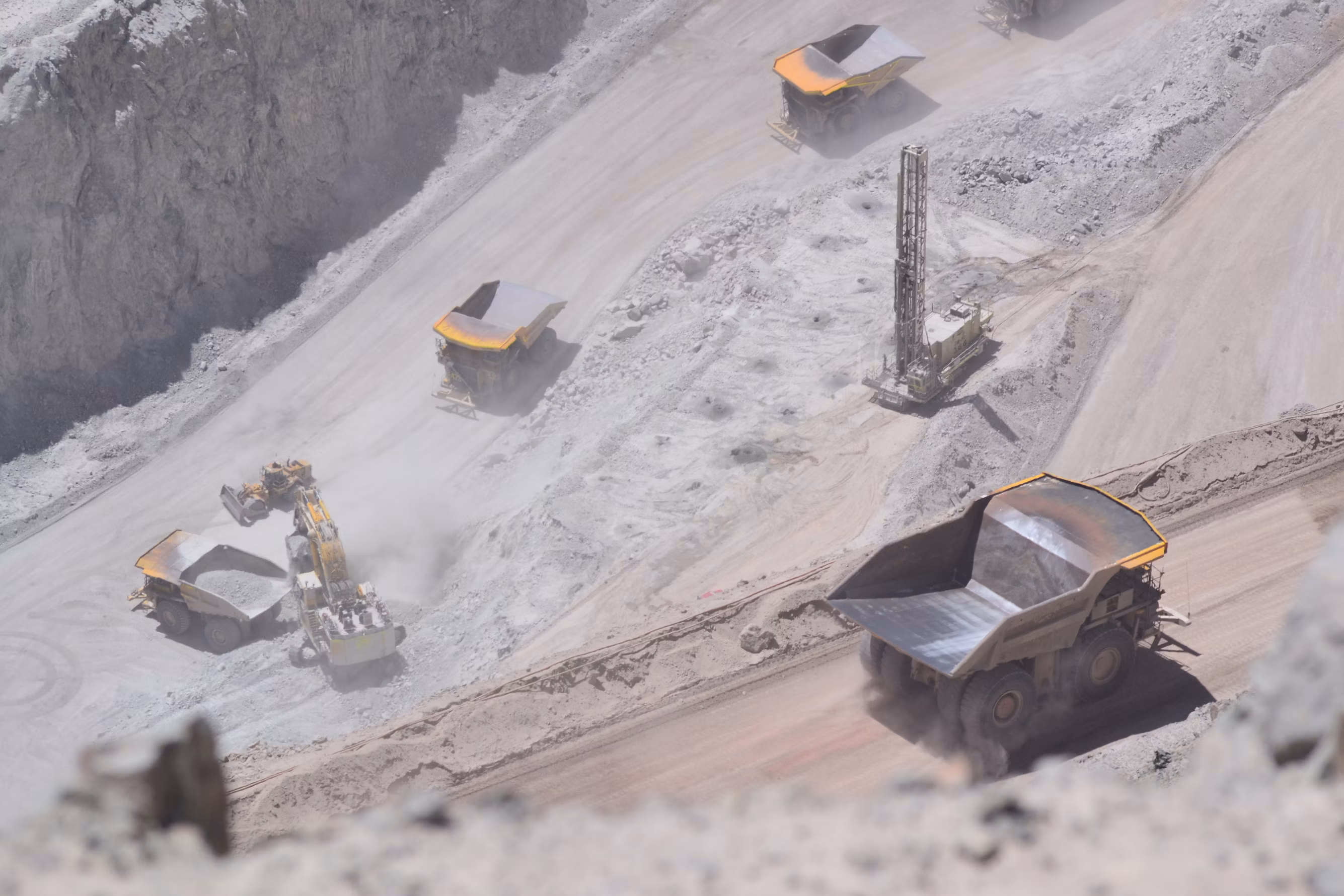 Massive open-pit mineral mine with large heavy haul dump trucks and drilling rigs moving along benches