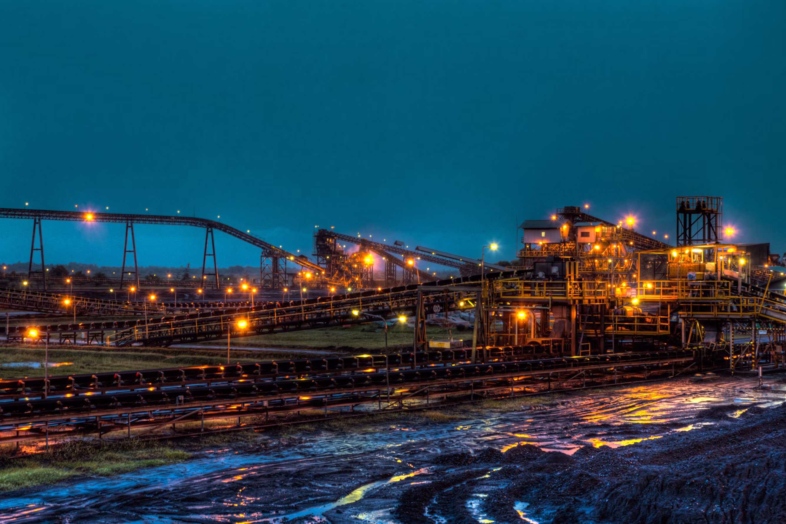 Illuminated industrial mineral export terminal and overland conveyor system at dusk with vibrant blue sky